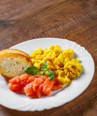 Scrambled eggs with smoked salmon and toast in white plate on wooden table background