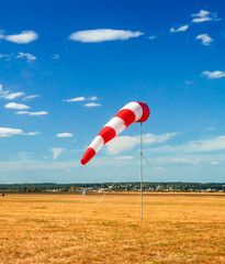 red and white windsock wind sock on blue sky on the aerodrome, yellow field and clouds background in autumn
