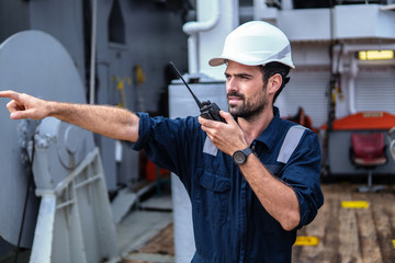 Marine Deck Officer or Chief mate on deck of vessel or ship . He holds VHF walkie-talkie radio in...