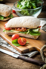Ciabatta sandwich with arugula salad, bacon and yellow cheese.