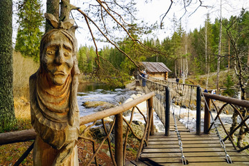 Carved wooden sculpture of an old woman near the pedestrian suspension bridge over a waterfall on...