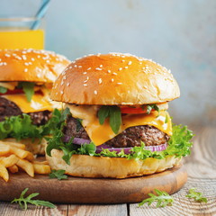 Two fresh homemade burgers with fried potatoes and orange juice on a wooden table
