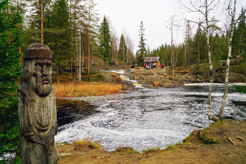 Carved wooden sculpture of an old man near the waterfall on the river tokhmayoki.