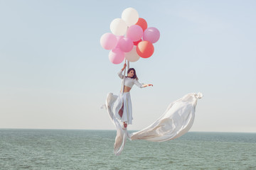 Young woman flying in the air by balloons.