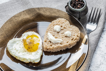 Heart shaped fried egg and bread in a plate, on a set table. Smiley on a piece of bread.