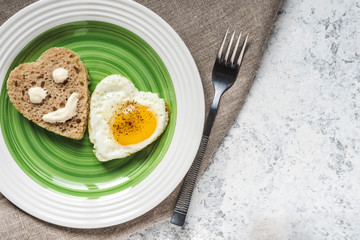 Fried egg and bread in the shape of a heart. Smiley on a piece of bread.