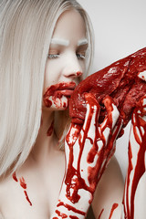 Young blonde eating fresh bloody meat. The hands and face of the girl with traces of blood