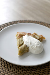 Slice of sweet rhubarb pie served with sweetened whipped cream. Selective focus. 