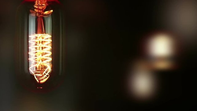 turn on and turn off in slow motion, retro vintage light bulb with old technology with filament built-in with warm light yellow tint and black background with unfocused retro bulbs, vintage object