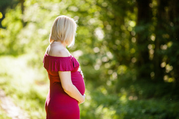 Portrait of beautiful pregnant woman in stylish long purple maternity dress looking dreamy in the middle of forest