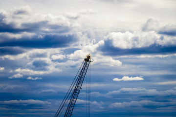 A crane in the harbor of Oslo on a cloudy summer day in Norway. The crane is used to load and unload cargo for small ships. The sky in the background has some fantastic structures.