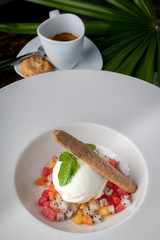 Beautiful presentation of vanilla ice cream and mixed fruit in white dish with cup of espresso in background