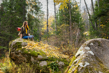 Young girl sits on a rock on a forest background.