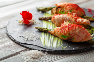 Asparagus rolled with chicken meat slices served on dark plate