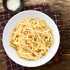 Traditional Italian Spaghetti Carbonara served on plate, grated cheese on the side, photographed overhead on rustic wood (Selective Focus, Focus on the top of the dish)