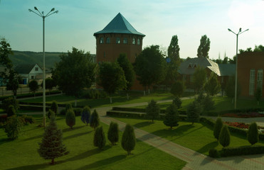 The high hexagonal tower of red brick and other buildings in the city park in the summer.