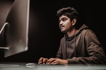 Handsome indian man hacker stole data from computer on internet, black background.
