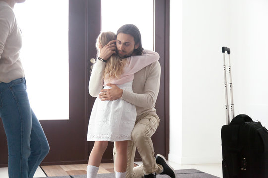 Married couple and little daughter in hallway at home. Sad unhappy father hugs small daughter. Parents divorcing, break up, child stay with mother, dad leave with suitcase. Discord in family concept