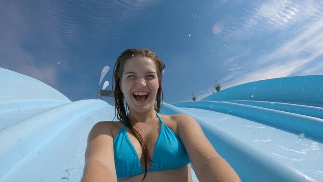 Teenage girl filming herself going down on a waterslide and having fun in slow motion