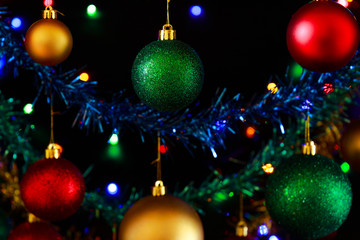 Close up of hanging Christmas decorations against a black background.