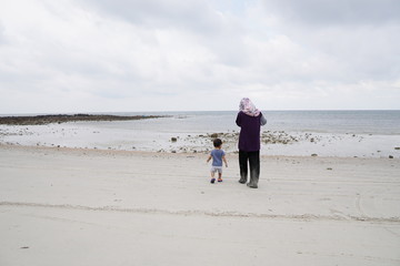 Asian Muslim mother and her son walking by the sea beach. Family concept.