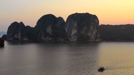 Aerial image of Halong Bay during golden our with fisher boat in the foreground and the iconic limestone karsts in the background. A UNESCO world heritage site.