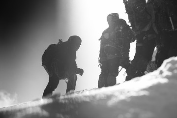 Silhouettes of climbers on a snow-covered mountain slope. Black-and-white.