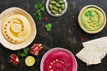 A variety of colored hummus, pita bread, olives, pomegranate on a dark woody background. Top view,...