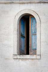 An arched window with semi open shutters on a white wall