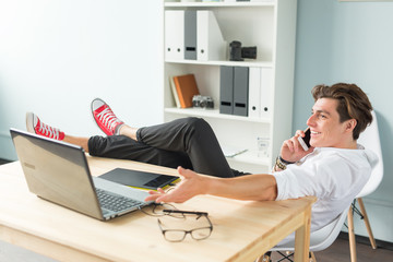 Business, people and fun concept - handsome man talking on mobile phone and puts feet up on table in the office.