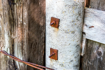 Old boards are fastened with rusty bolts with nuts and washers to the concrete pillar