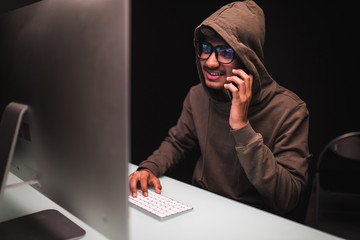 cybercrime, hacking and technology concept. Indian man hacker talk smartphone and coding on...
