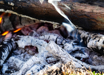 Fototapeta na wymiar Smoldering embers of fire with log in smoke, close up