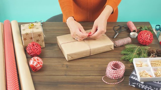 Christmas flat lay of unready hand crafted gift box on rustic wooden table with rolls of craft and colour wrapping paper, pine cones, fir branches and decor elements.