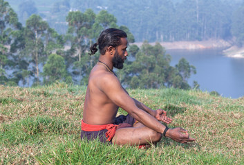Indian man meditating in lotus yoga pose on green grass in Kerala, South India