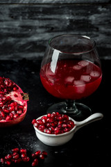 Tempting pomegranate, red seeds and fresh juice with the addition of ice on a black, stone...