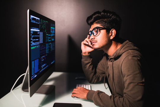 Thoughtful young indian programmer coding on computer in the evening at home