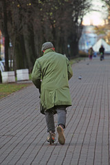 a man in a green coat riding a scooter on an autumn boulevard