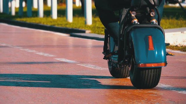 People Riding an Electric Scooter on Bike Path in the Park. Slow Motion in 180 fps. Red asphalt road for cyclists with markings and Palm Trees in the Resort City. Summer, sunny day.