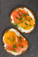 Delicious bread toasts with cream cheese (ricotta), salted smoked salmon, tangerine and pea sprouts. Gourmet snack