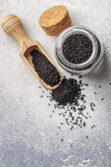 Black cumin seeds on a wooden spoon and in a glass jar on gray background