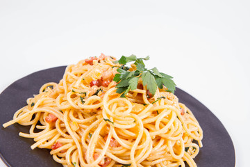 Spaghetti Carbonara with some parsley on a black plate on a white background