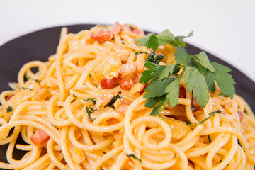 Spaghetti Carbonara with some parsley on a black plate on a white background