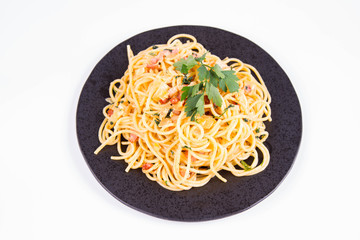 Spaghetti Carbonara with some parsley on a black plate on a white background