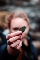 A girl finding old polished glass in a river bank of a mountain river and holding the glass piece in the hand with blurry background and shallow depth field. Okertal, Okertalsperre, Oker (Goslar) Nati