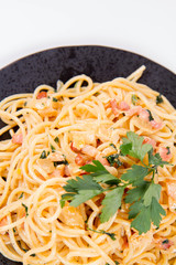Spaghetti Carbonara with some parsley on a black plate on a white background