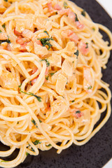 Spaghetti Carbonara with some parsley on a black plate on a white background