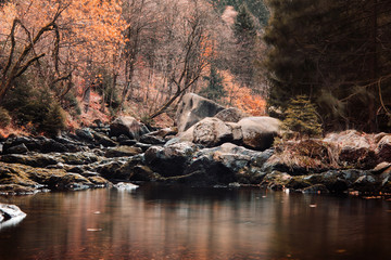 Beautiful calm mountain river with giant rocks on the river banks and autumn color leaves in the forest background. Okertal, Oker gorge, Oker National Park Harz, Harz Mountains, Germany
