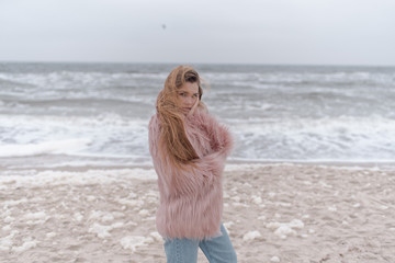 Beautiful girl in a fur coat on the beach of the ocean
