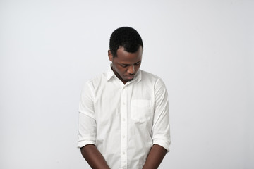 Shy young handsome african man feels awkward isolated on grey wall background.